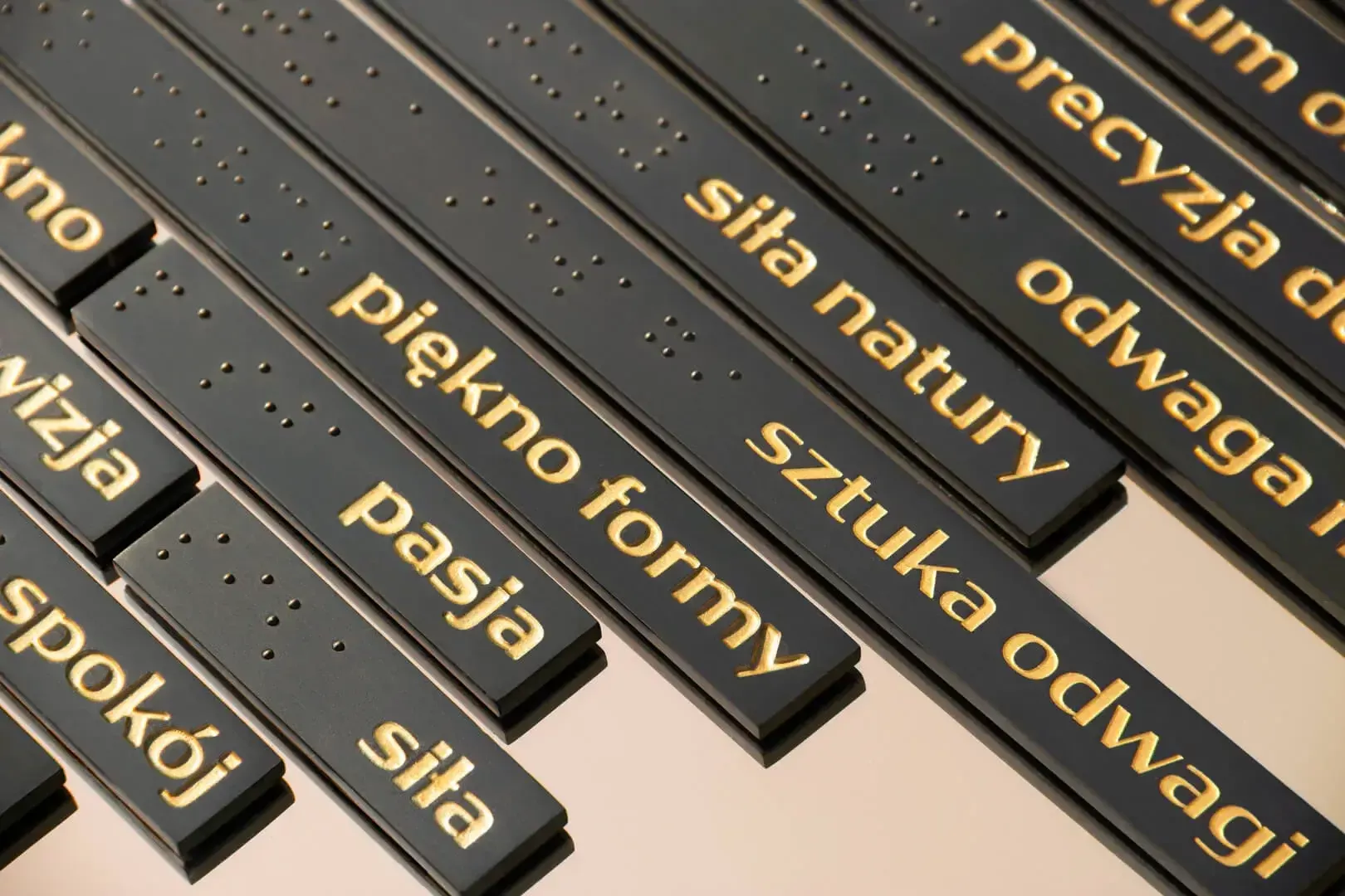 Tabliczka informacyjna - złote litery na czarnej tabliczce oraz zapis alfabetem Braille’a