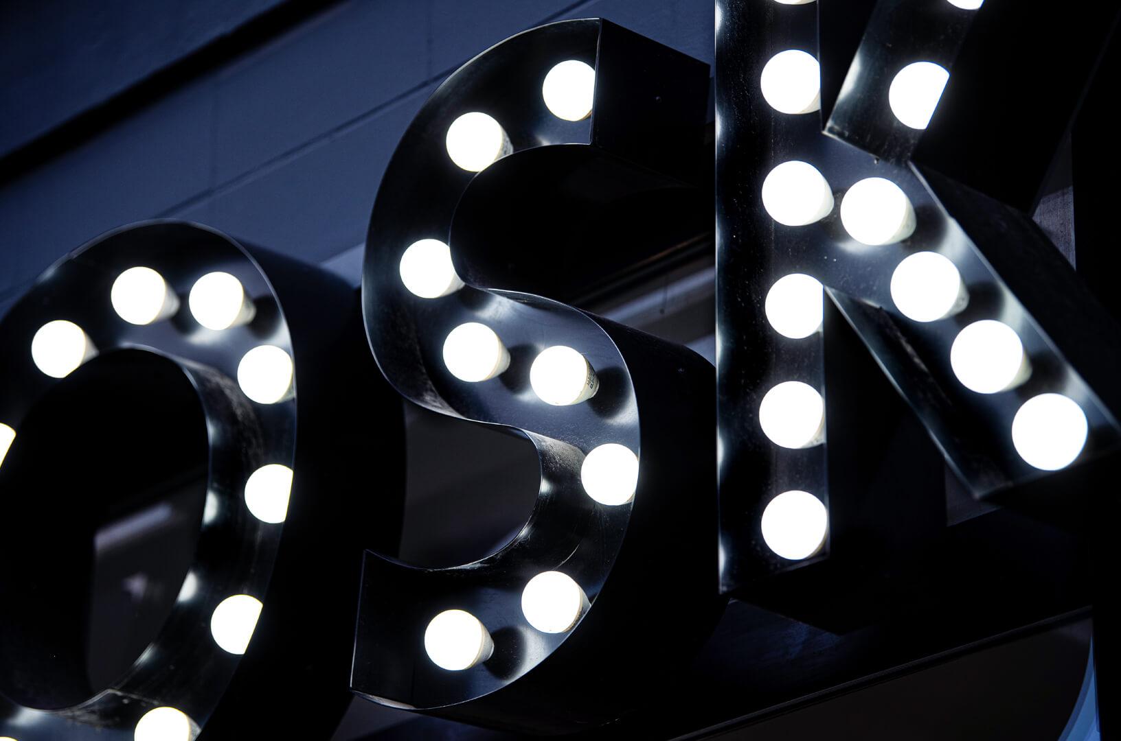 Letters with bulbs forming the word WOSK, white bulbs embedded in black letters