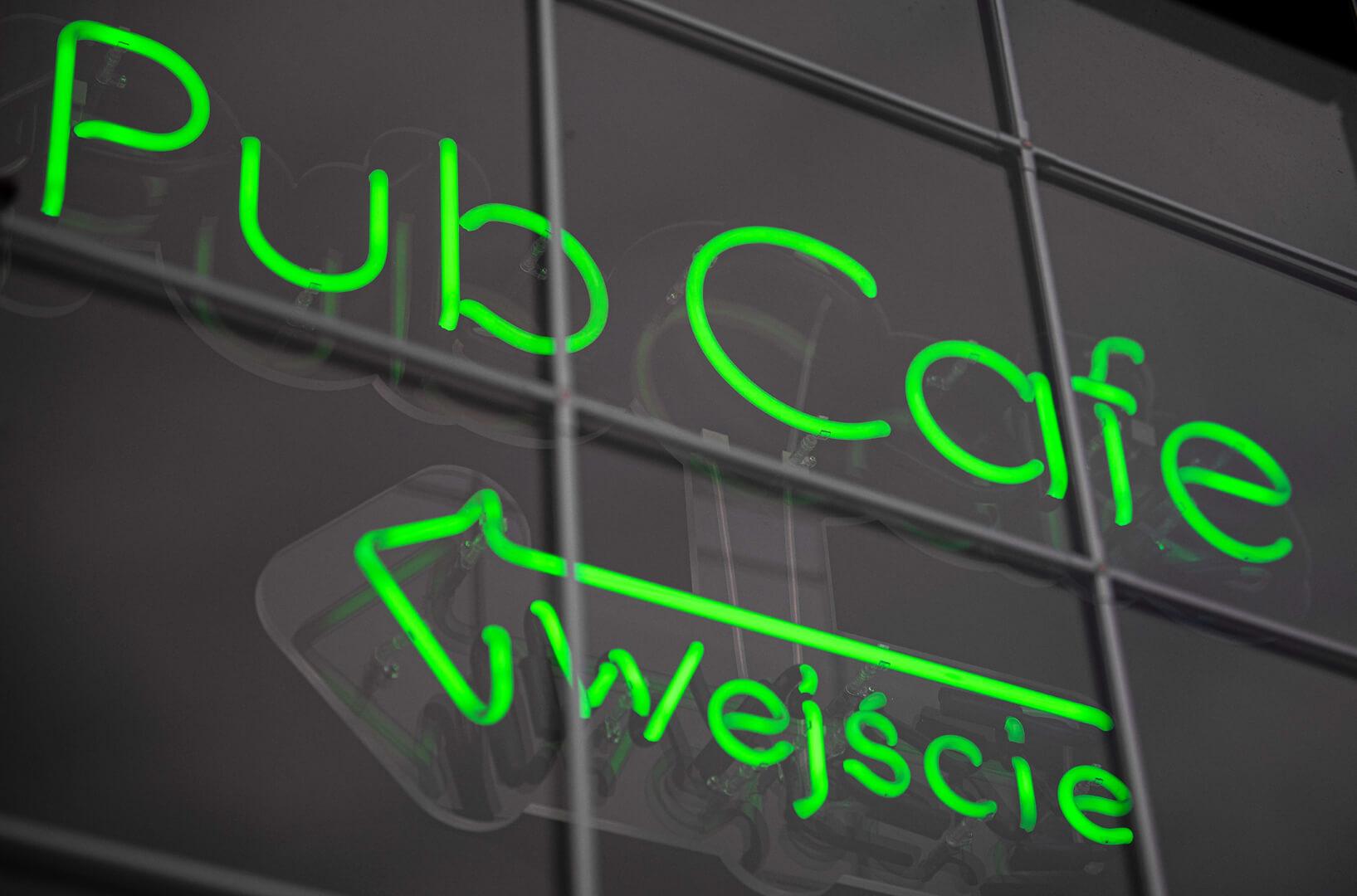 Green neon Pub Cafe sign with directions to the entrance.