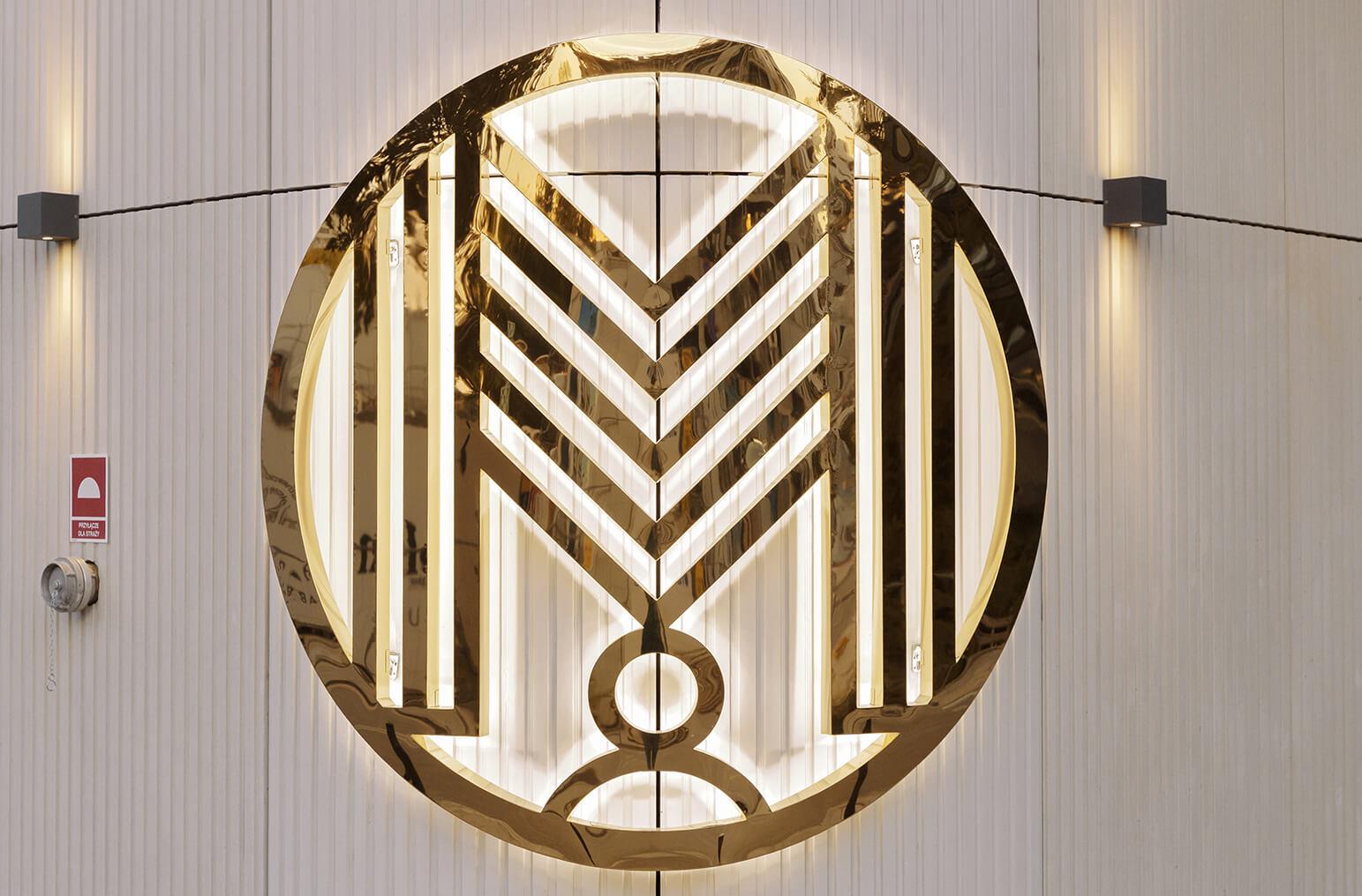 Back-lit logo on the wall, rounded in an arc, made of stainless steel.