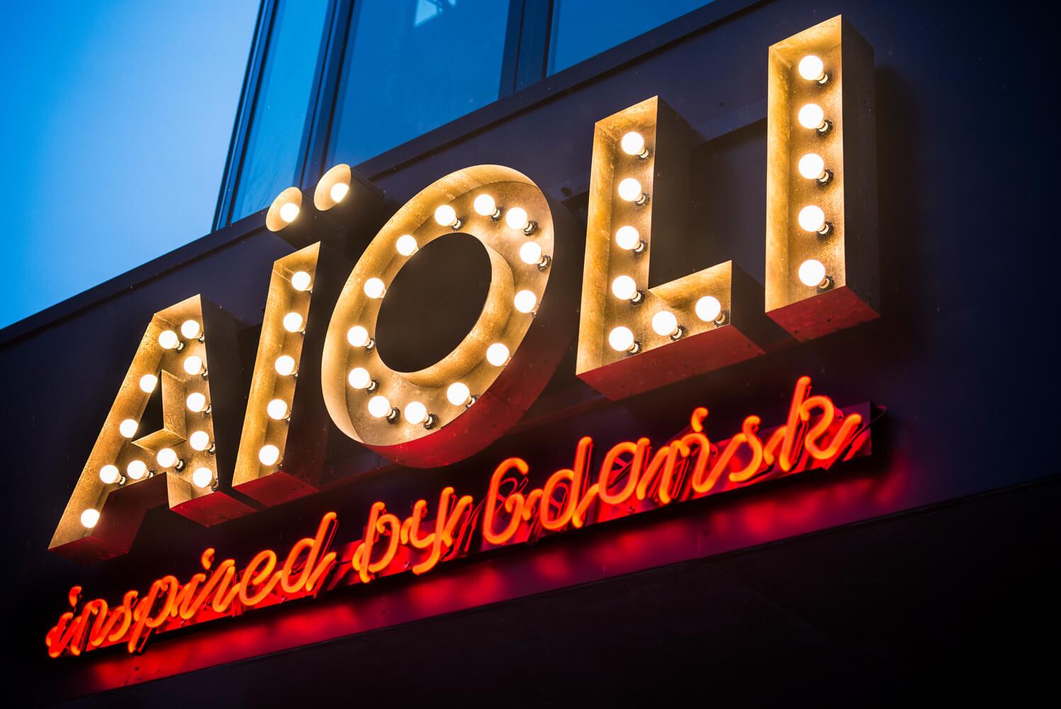 Aioli - Firmenschild bestehend aus Buchstaben mit Glühbirnen über dem Eingang