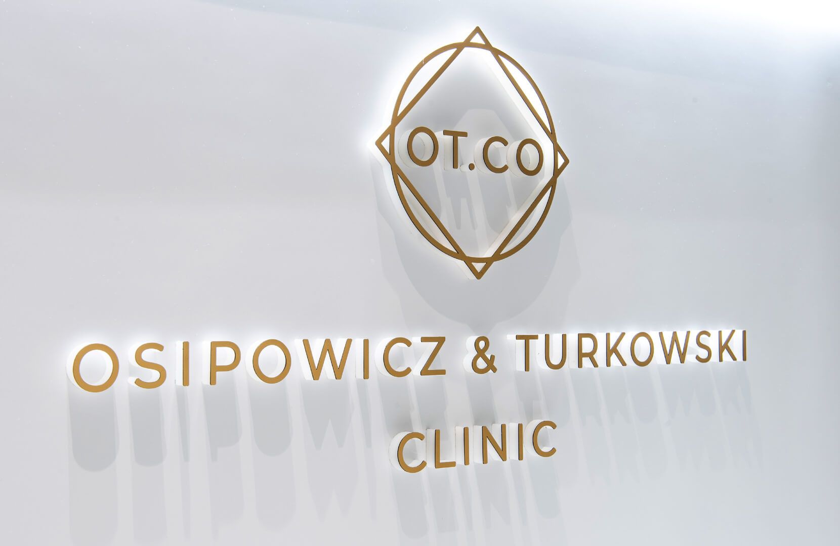 3D-Buchstaben an der Rezeption der OT.CO Klinik - Dreidimensionale goldene Buchstaben mit Logo an der Rezeption der OT.CO Klinik
