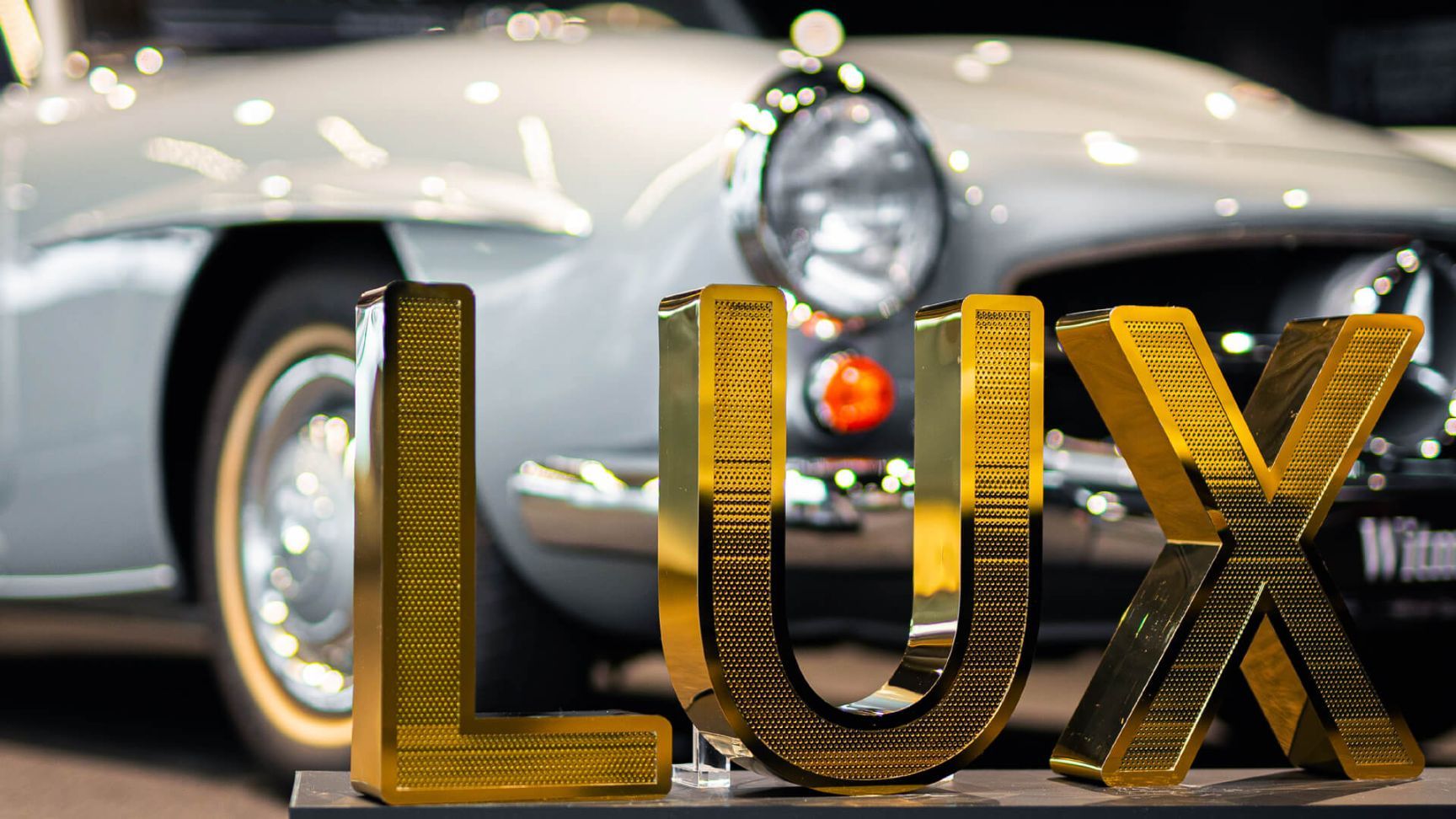 LUX-Buchstaben aus perforiertem Edelstahl - LUX-Schriftzug aus goldglänzendem, perforiertem Edelstahl, im Mercedes-Showroom