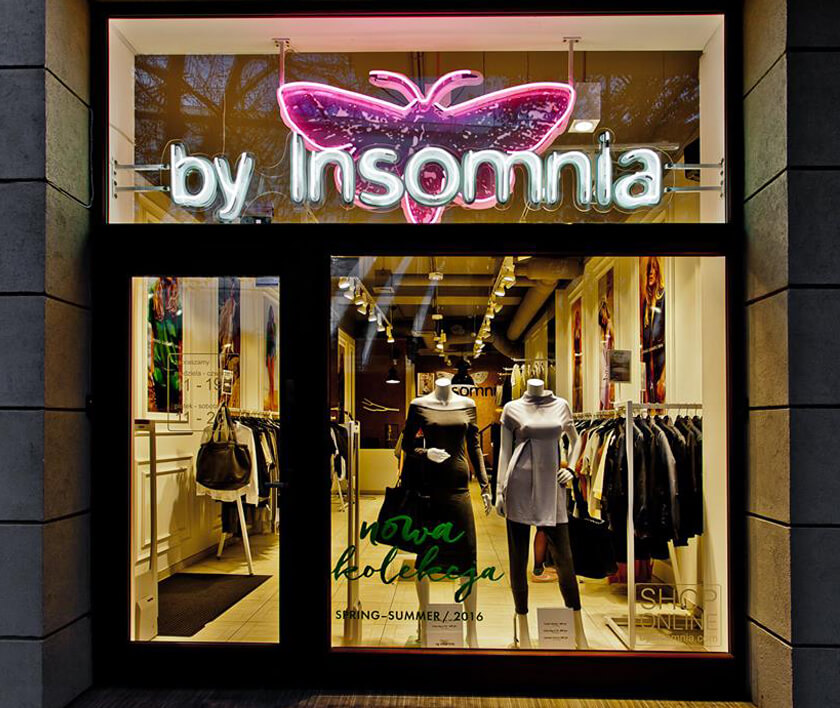 By Insomnia - letrero de neón con el nombre de la empresa, montado sobre plexiglás, colocado detrás de la ventana de cristal