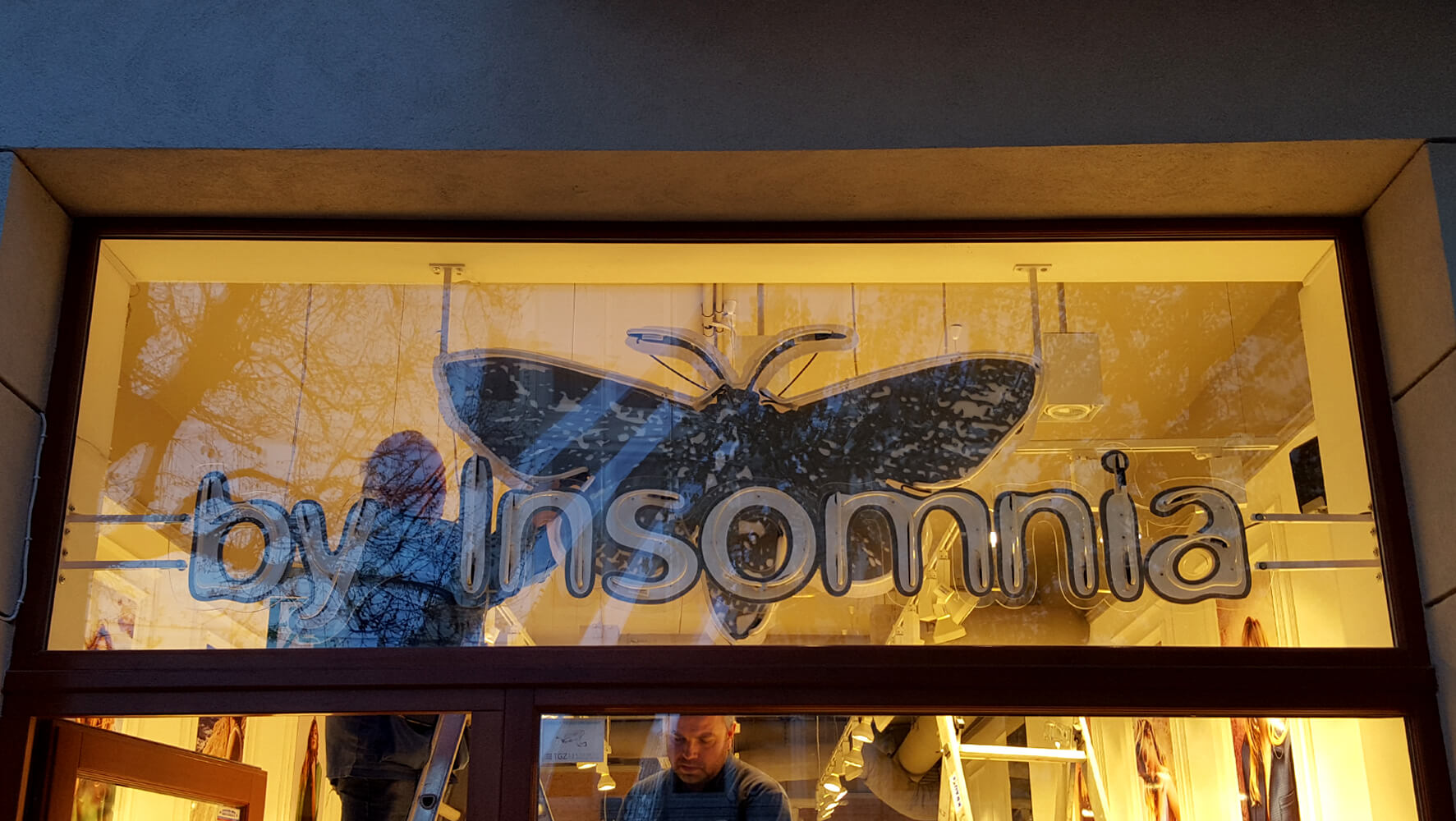 By Insomnia - Leuchtreklame mit dem Firmennamen, montiert auf Plexiglas, hinter dem Glasfenster angebracht