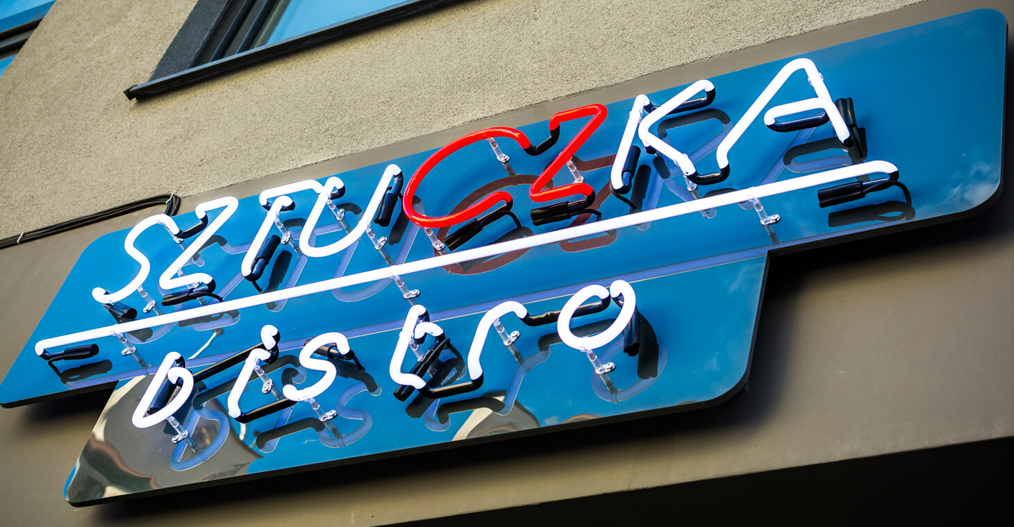 Sztuczka Bistro - neon reklamowy, zamontowany na płycie plexi, umieszczony nad wejściem