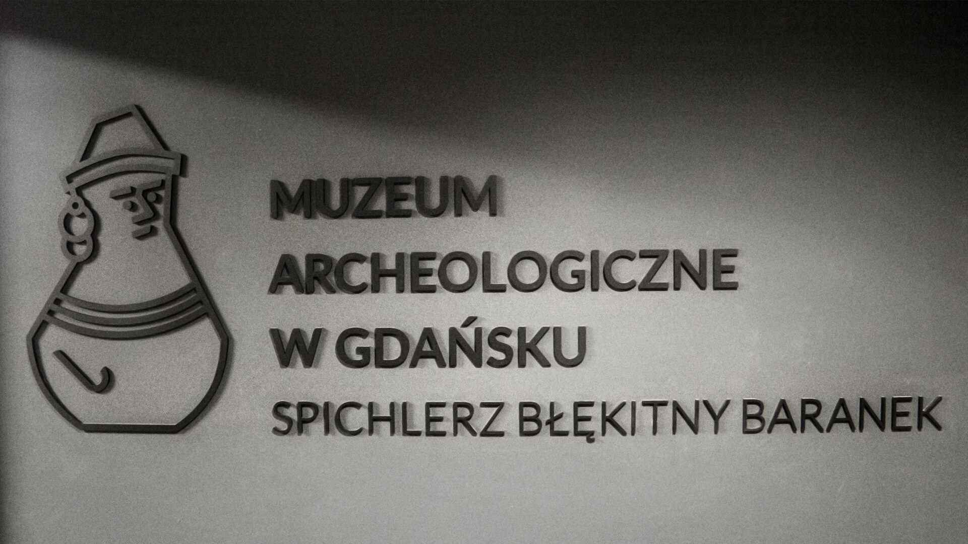 museum-archäologie-blauer-fass-schriftzug-an-der-wand-mit-ziegel-innen-bind-empfang-schwarzer-schriftzug-für-bestellung-mattes-logo-fest