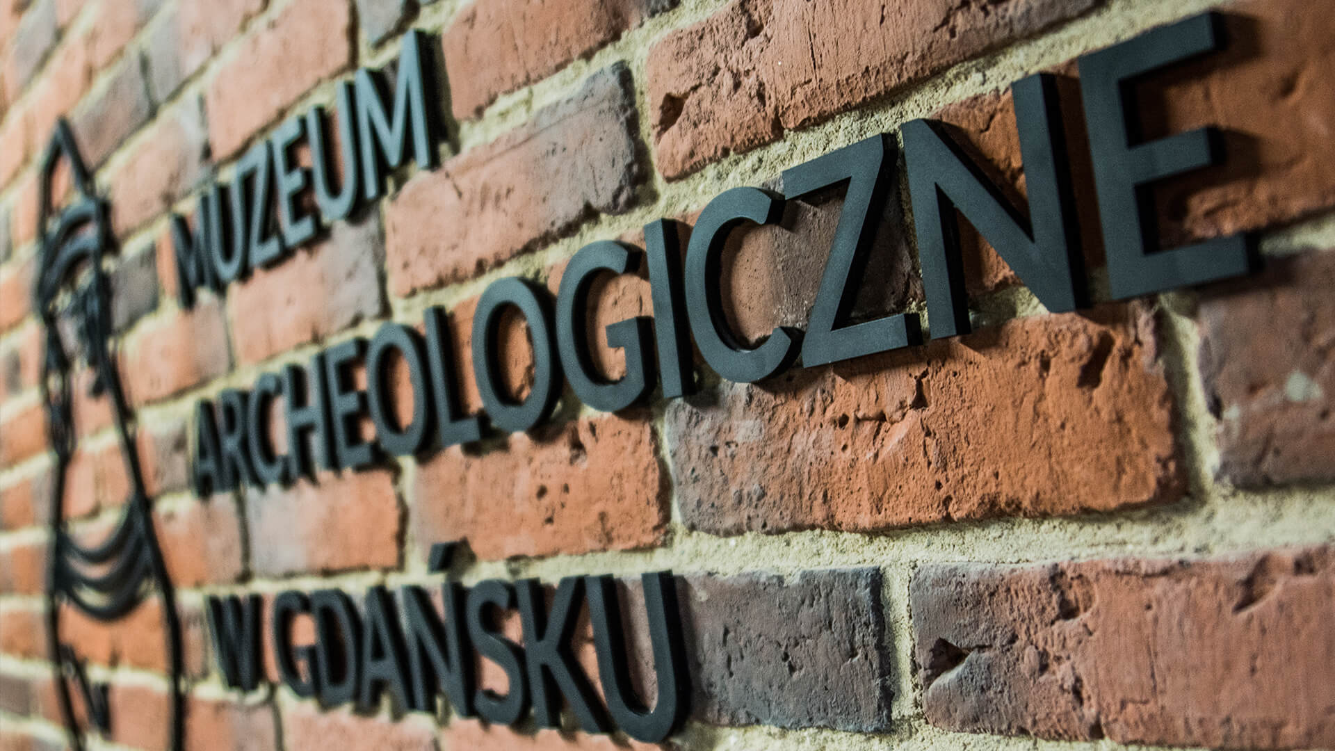 museum-archäologie-blauer-fass-schriftzug-an-der-wand-mit-ziegel-innen-bind-empfang-schwarzer-schriftzug-für-bestellung-mattes-logo-fest