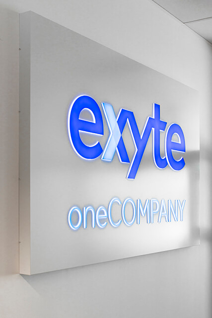 exyte-cashboard-on-the-wall-interior-of-the-office-behind-the-reception-blue-logo-back-lit-cashboard-for-order-gdansk-park-technological-scientific