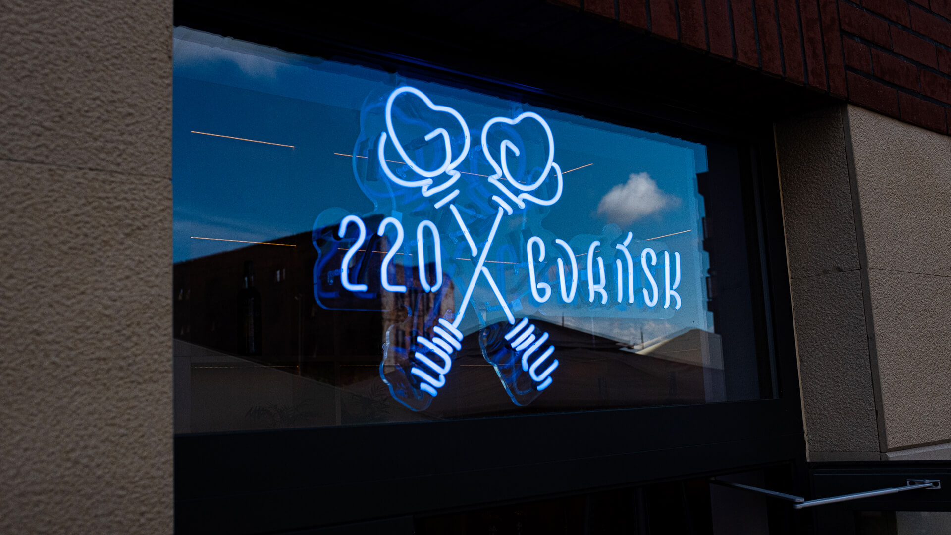 Neon 220 Gdańsk wraz z logiem za szybą nad drzwiami.