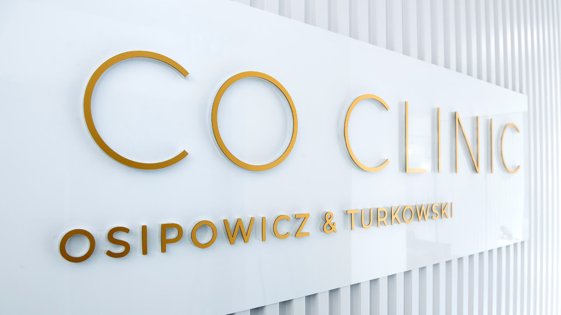 Gold prismatic letters on the wall in the reception area of OT.CO Clinic