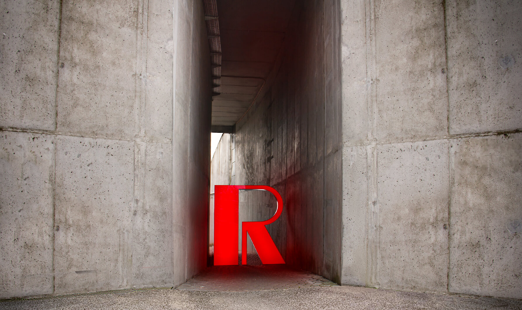 Lettera R di grande formato in rosso su una parete di cemento, illuminata a LED.