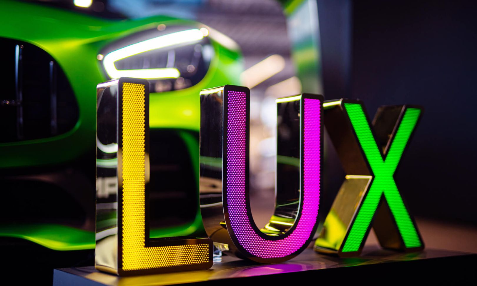 LUX belettering in geperforeerd roestvrij staal, verlicht met LED in drie kleuren, op een Mercedes-achtergrond