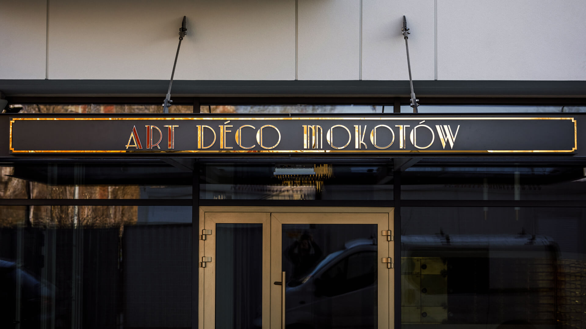 Art Deco Mokotów - Goldfarbene Dibond-Kassette über dem Eingang.