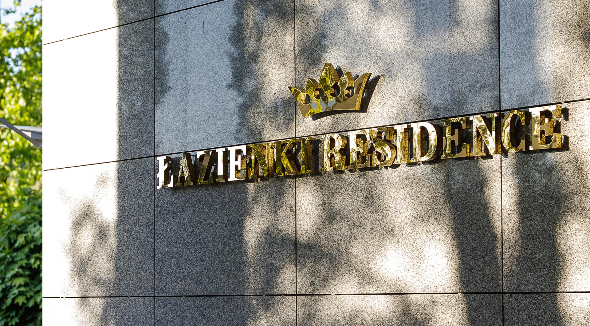 Łazienki Residence - Napis Łazienki Residence wykonany z blachy nierdzewnej w kolorze złotym, z koroną w logo.