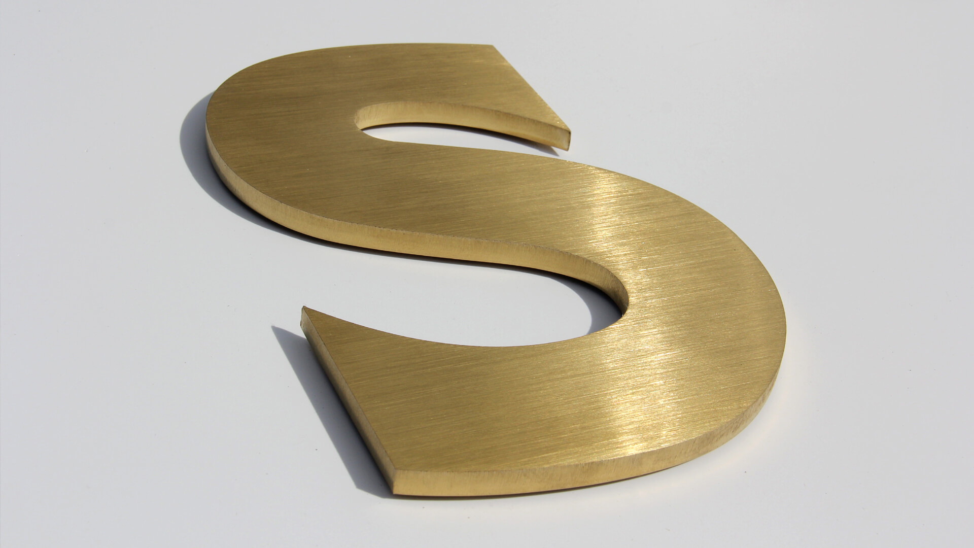 Złota litera S - Metalowa litera S w kolorze złotym, styl industrialny.