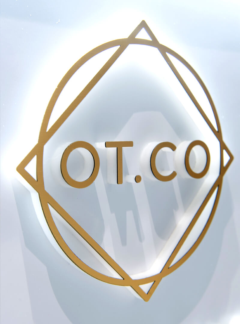 Logos an der Rezeption der OT.CO Klinik - Goldfarbenes Logo auf dem Empfangstresen der OT.CO Klinik.