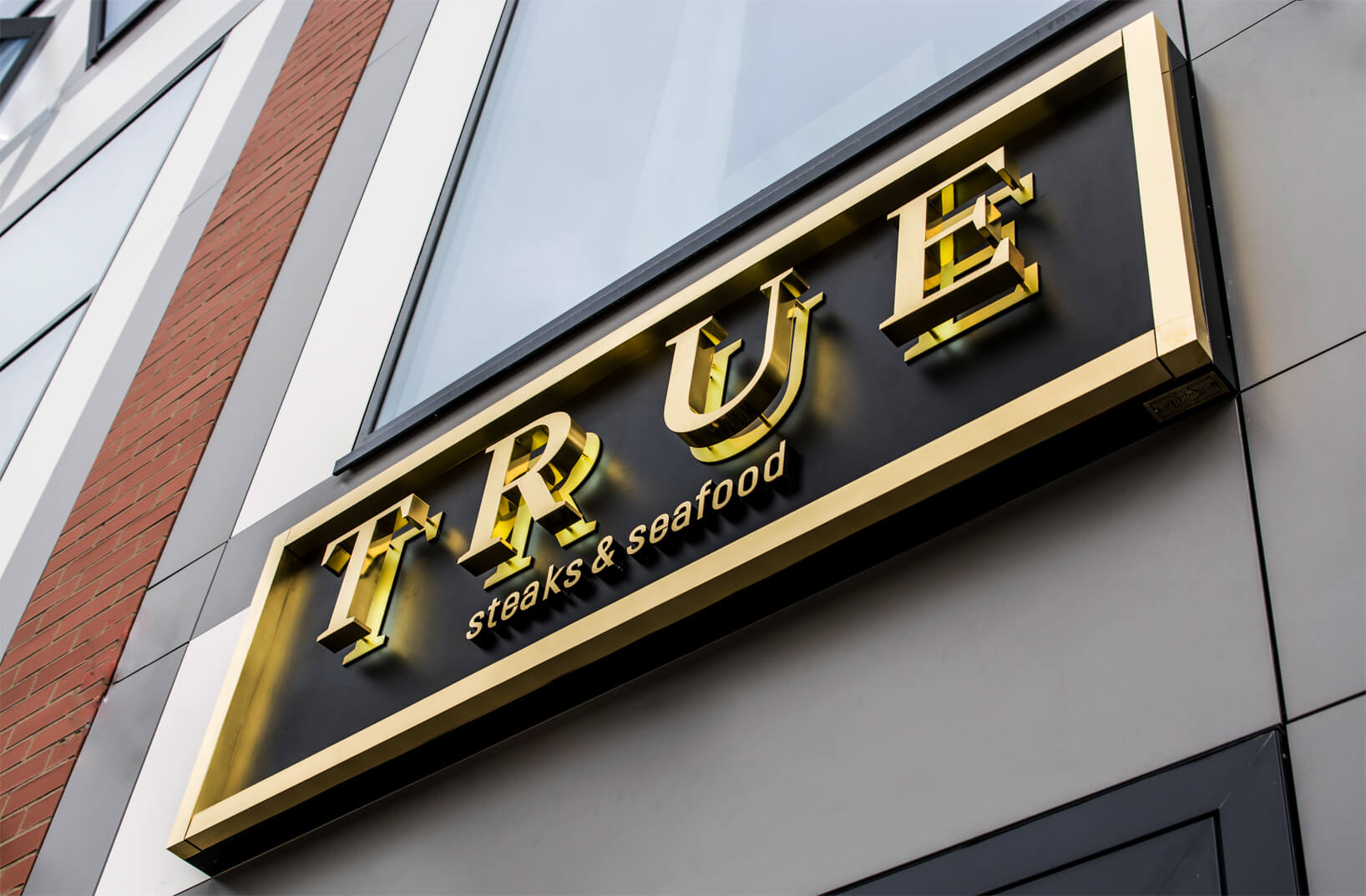 TRUE - True - external sign with golden letters made of stainless steel