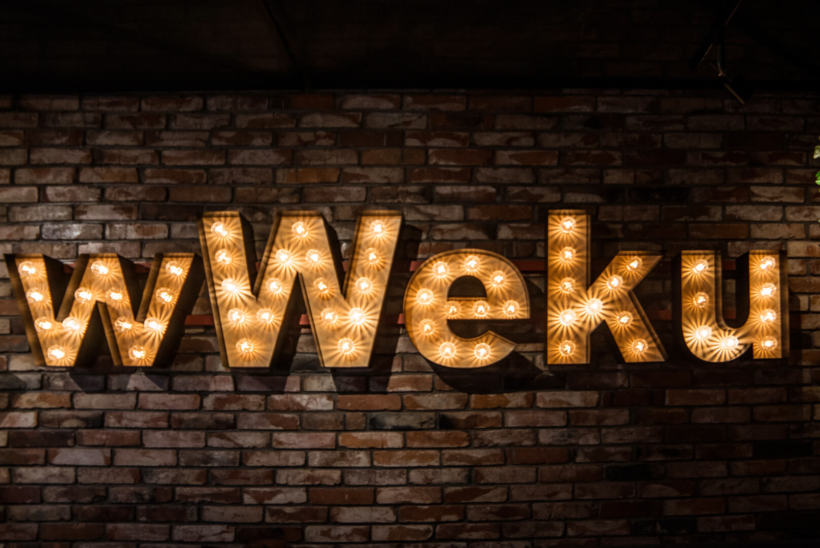 wWeku - wWeku - letras con bombillas colocadas en una pared de ladrillos