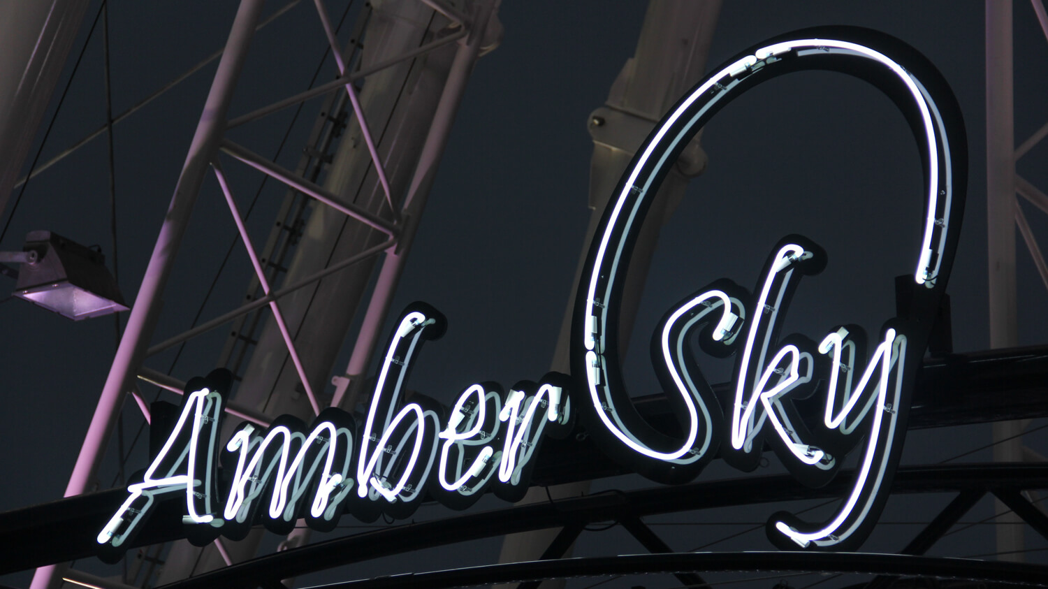 Bernsteinfarbener Himmel - Amber Sky - weißes Neonschild mit dem Firmennamen auf dem Gestell