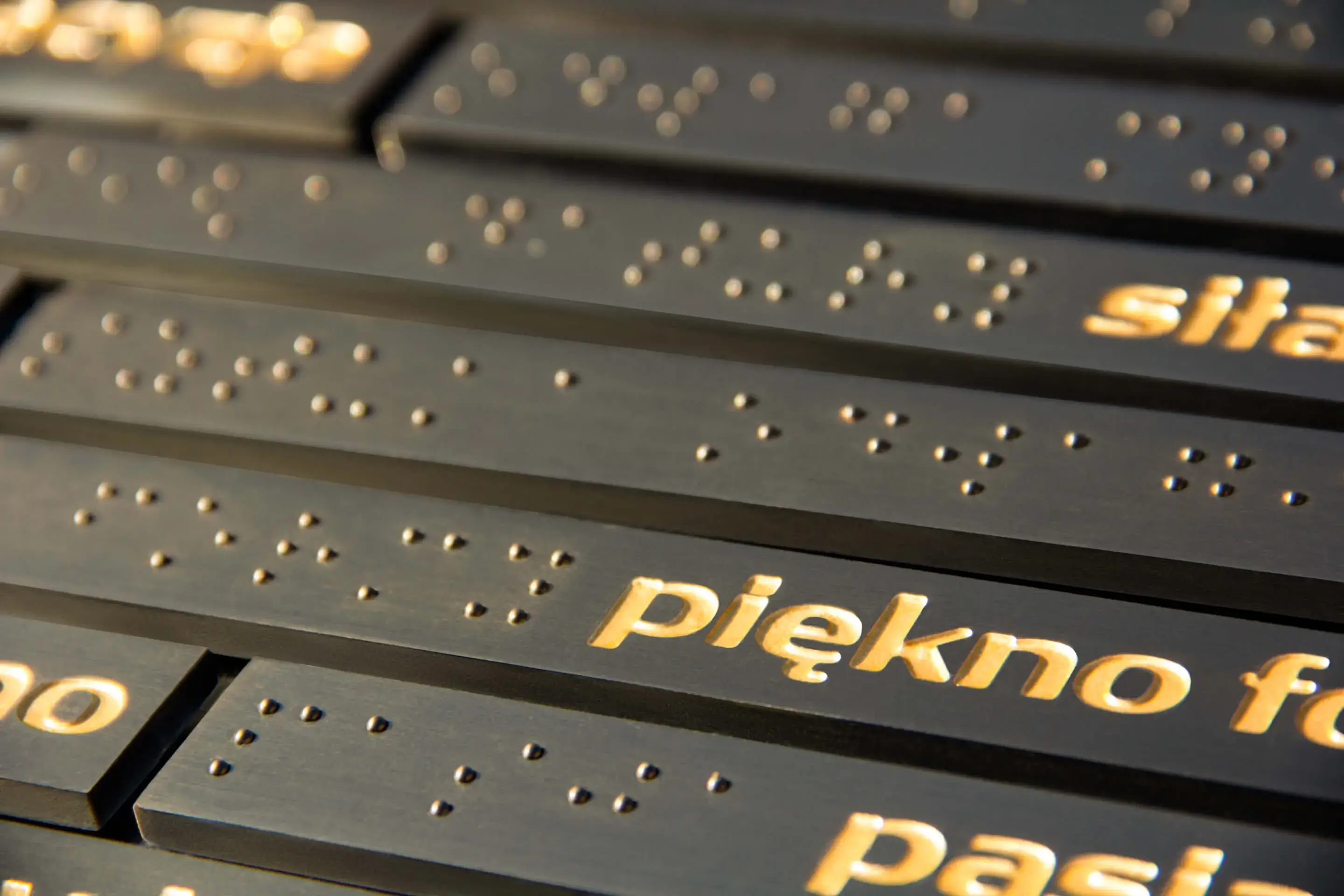 Tabliczka informacyjna - złote litery na czarnej tabliczce oraz zapis alfabetem Braille’a