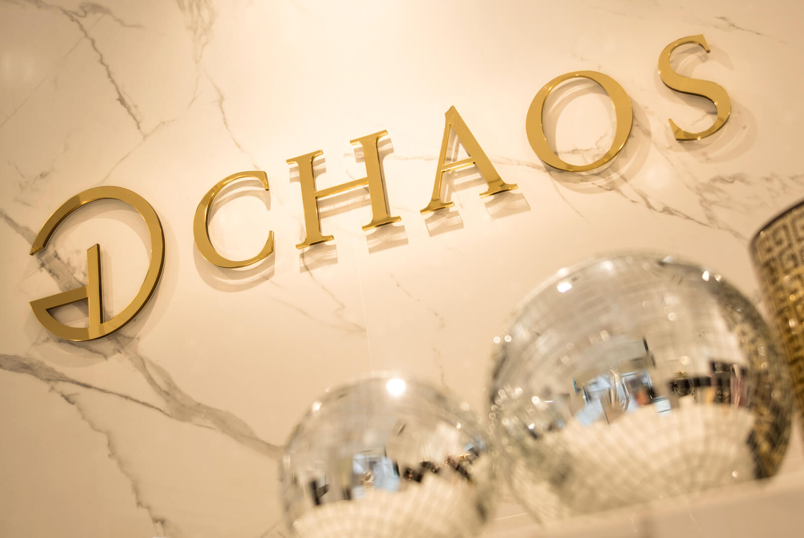 CHAOS - Chaos - logo en or et lettres en bloc 3D en plexiglas placées sur le mur.